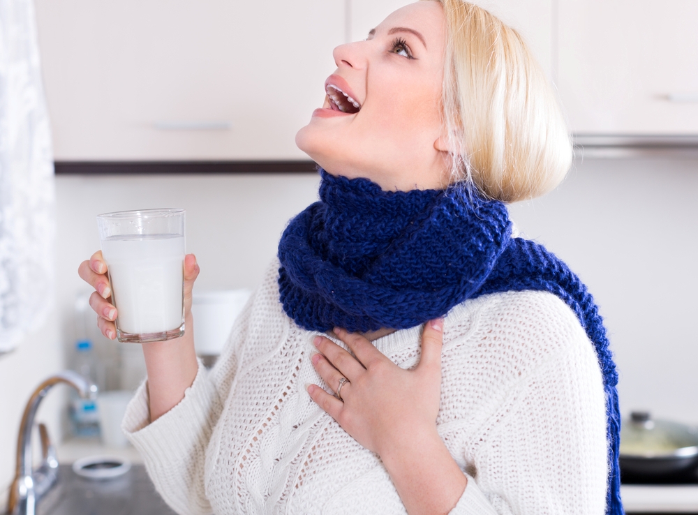 Blonde young woman having pain in throat and doing oral rinsing at kitchen